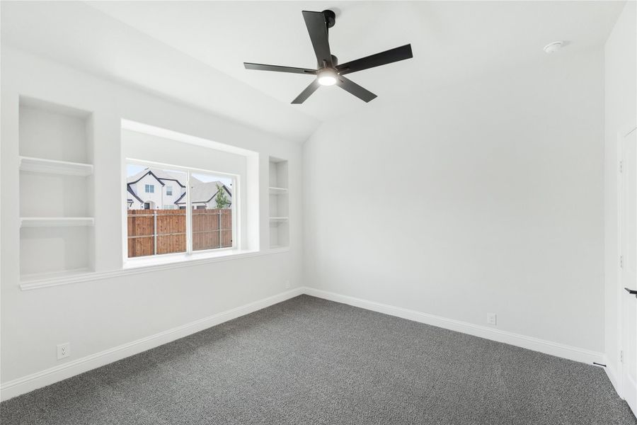 Empty bedroom with vaulted ceiling, black ceiling fan, built-in shelves, and gray carpet