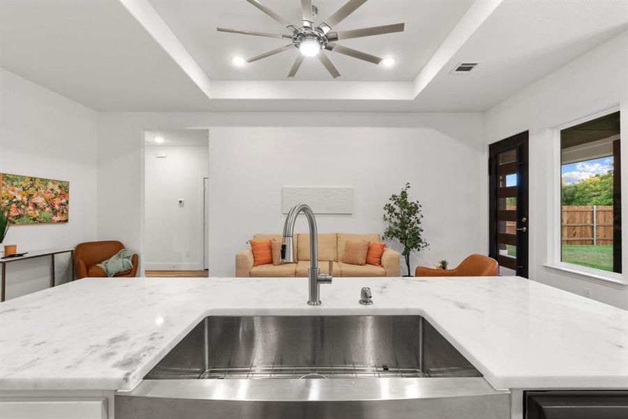 Kitchen featuring ceiling fan, a raised ceiling, light stone counters, and sink