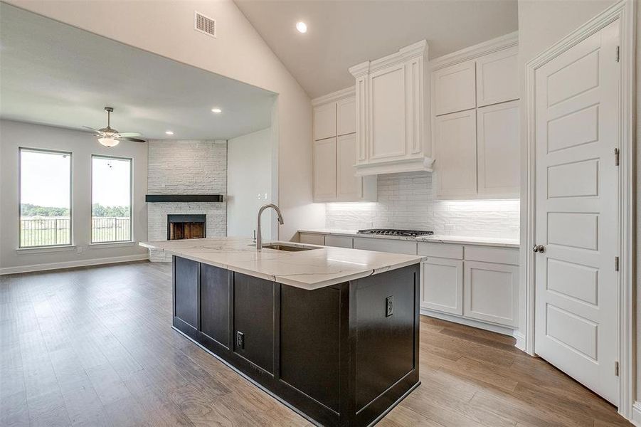 Kitchen featuring sink, white cabinets, vaulted ceiling, a center island with sink, and ceiling fan