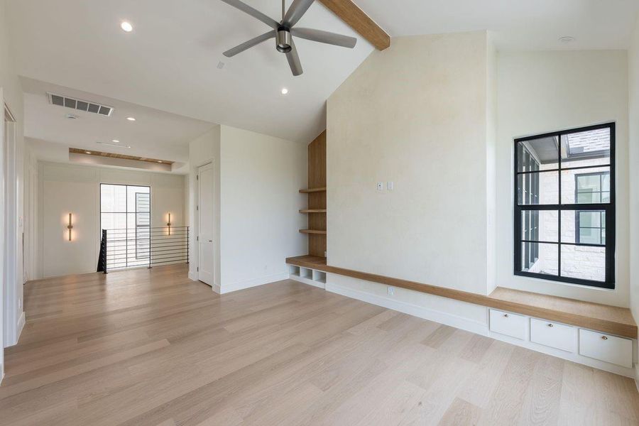 Bathed in natural light from expansive picture windows, this vaulted living space feels both serene and architectural. A floating bench with integrated storage, custom shelving, and a textured feature wall create a refined focal point designed for gathering and unwinding.
