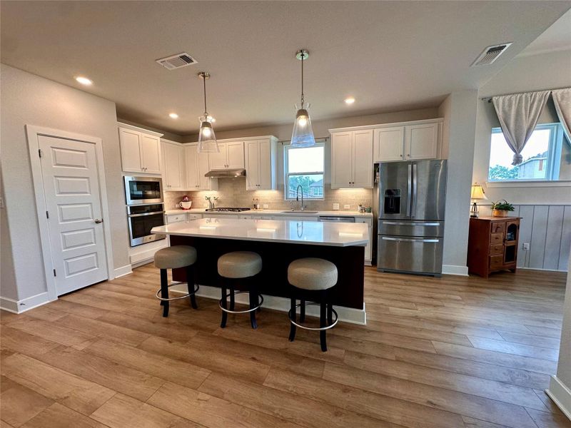 Modern kitchen featuring a central island with countertop seating, stainless steel appliances, white cabinetry, and wood-finish LVP.