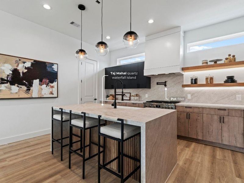 This kitchen is a showstopper with its double waterfall island wrapped in 5cm Taj Mahal quartz, accented by modern pendant lighting and fluted wood details—it’s all in the details with this home.