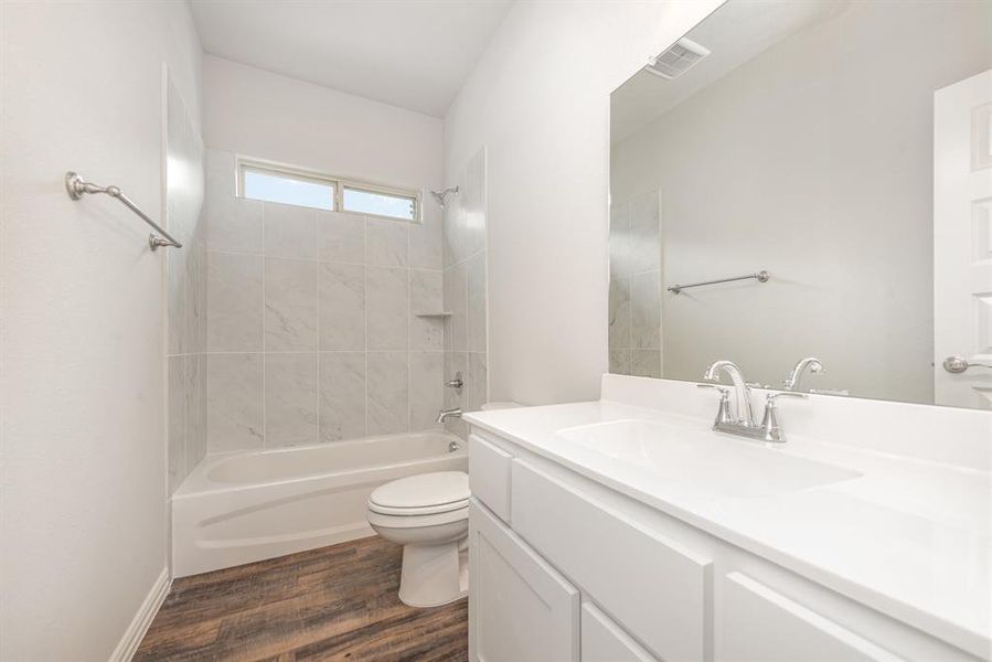 Full bathroom with vanity, toilet, tiled shower / bath, and hardwood / wood-style flooring