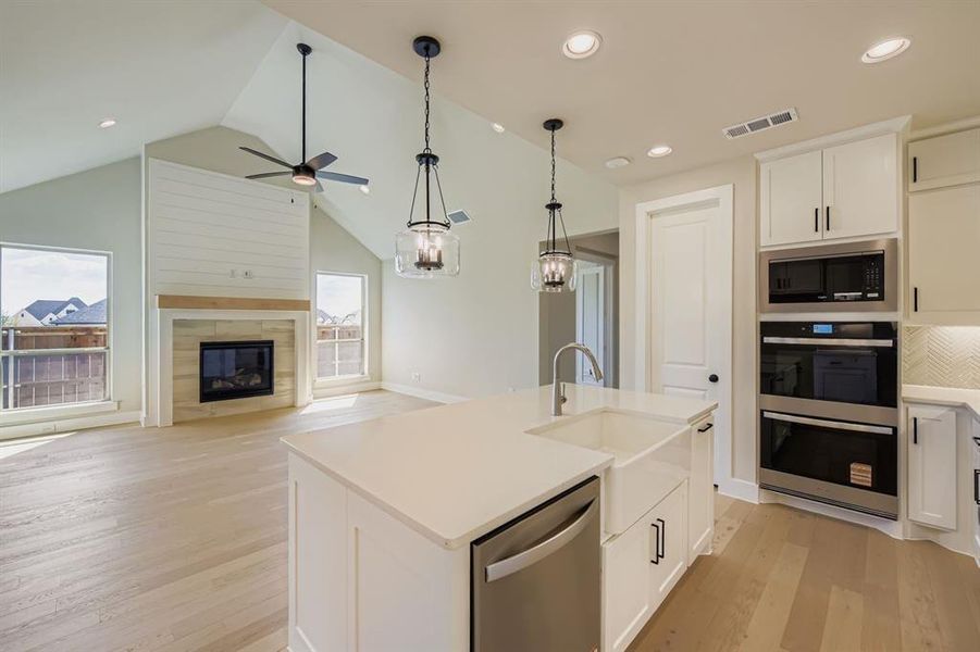 Kitchen with white cabinetry, stainless steel appliances, light wood-style floors, pendant lighting, and open floor plan