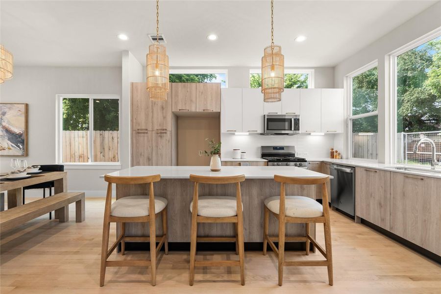Sunlit kitchen featuring two-tone European-style cabinetry, quartz countertops & stainless steel appliances, designed with a large island perfect for dining & entertaining.