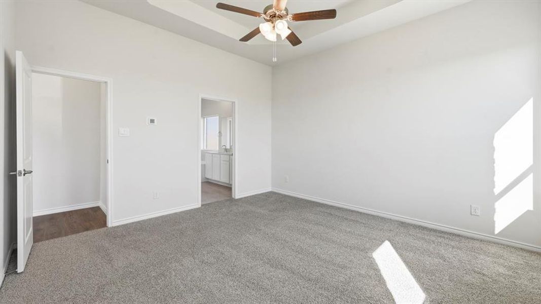 Unfurnished bedroom featuring carpet flooring, ensuite bath, ceiling fan, and a tray ceiling Unfurnished bedroom featuring carpet flooring, ensuite bath, ceiling fan, and a tray ceiling