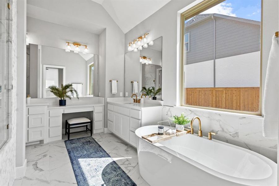 Full bath featuring a freestanding bath, vanity, vaulted ceiling, and light marble finish flooring