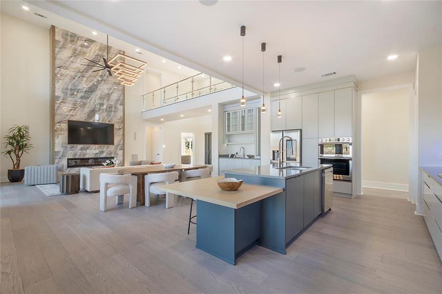 Kitchen with modern cabinets, open floor plan, light wood finished floors, a center island with sink, and a high end fireplace Kitchen with modern cabinets, open floor plan, light wood finished floors, a center island with sink, and a high end fireplace