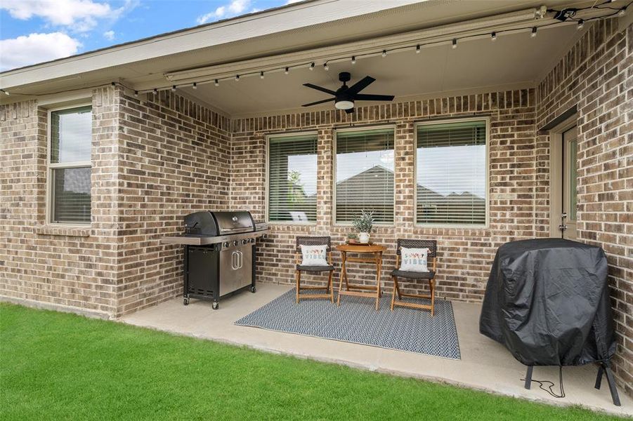The property features a covered patio with a ceiling fan, string lights, and a brick exterior, extending to a lawn area