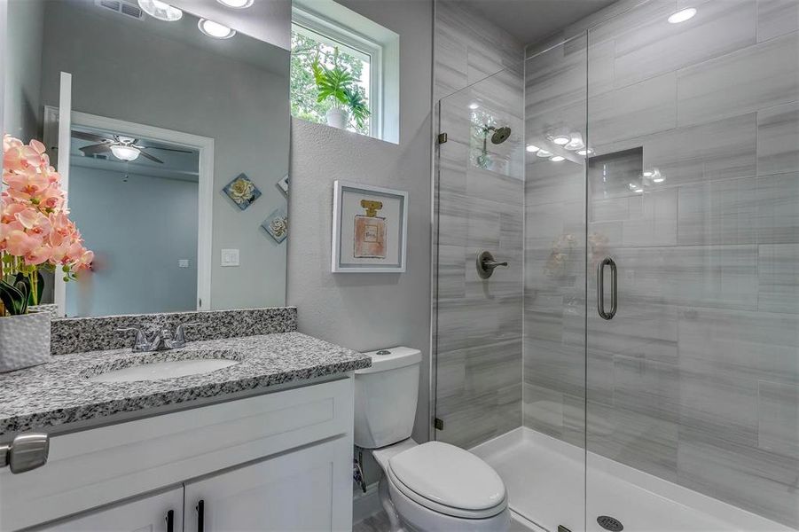 Bathroom with ceiling fan, vanity, a shower with shower door, and toilet