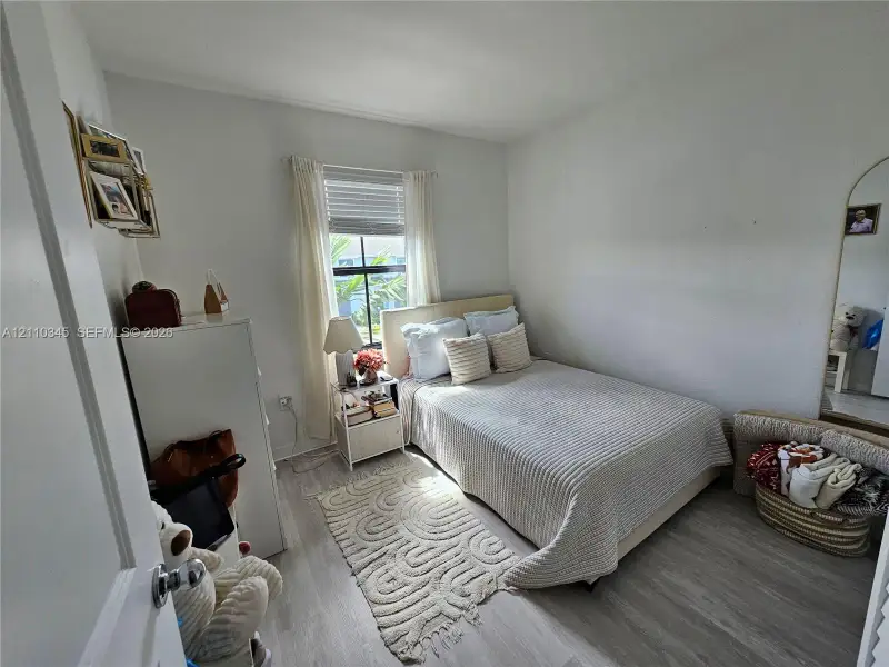 Bedroom featuring light-toned wood-finish flooring, neutral wall paint, and a window with horizontal blinds