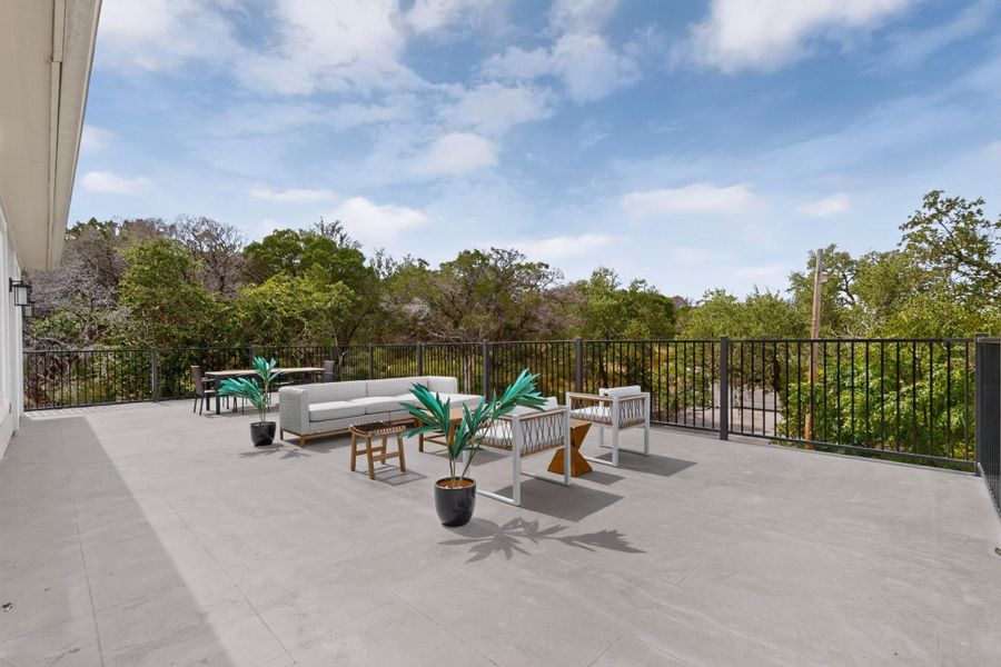 An expansive tiled patio overlooks surrounding mature trees and a clear blue sky.