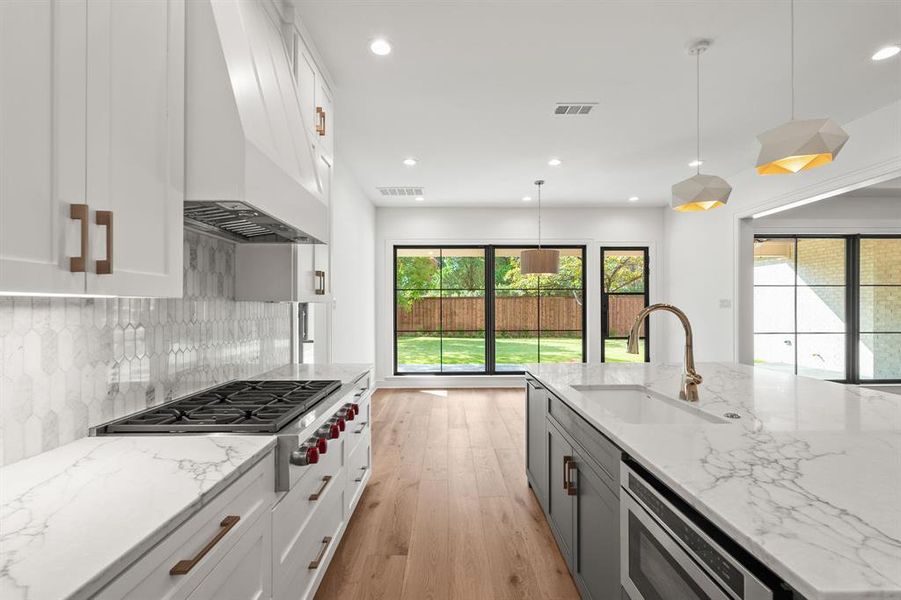 Kitchen with white cabinetry, light stone countertops, light wood finished floors, hanging light fixtures, and recessed lighting Kitchen with white cabinetry, light stone countertops, light wood finished floors, hanging light fixtures, and recessed lighting