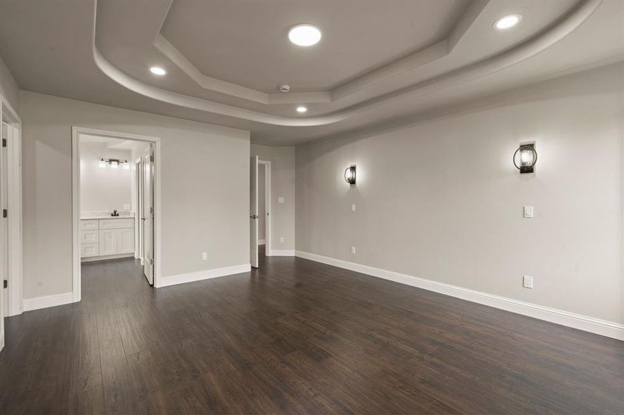 Unfurnished living room with a raised ceiling, dark wood finished floors, baseboards, and recessed lighting