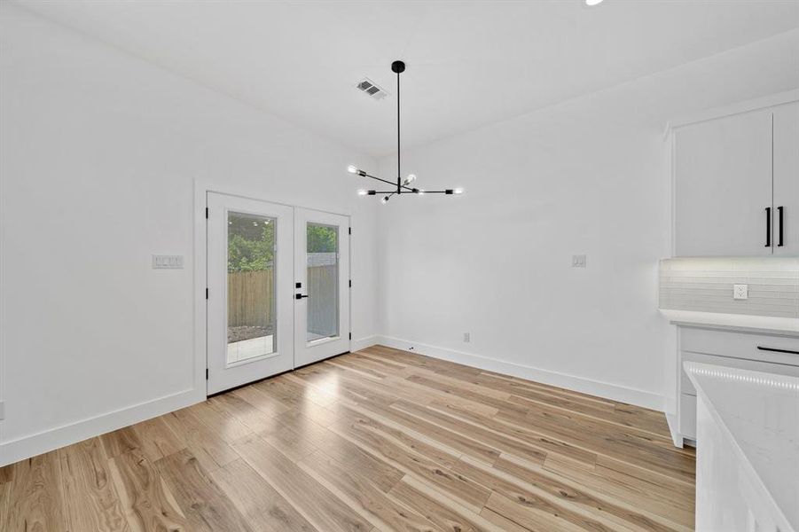 Unfurnished dining area with an inviting chandelier, french doors, and light hardwood / wood-style floors