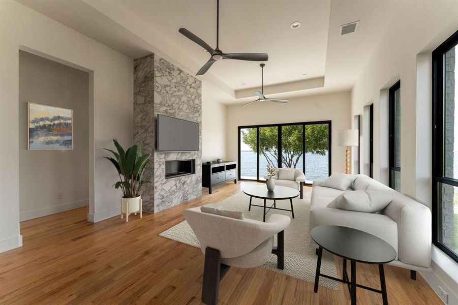 Living area featuring light wood finished floors, a premium fireplace, ceiling fan, and a raised ceiling