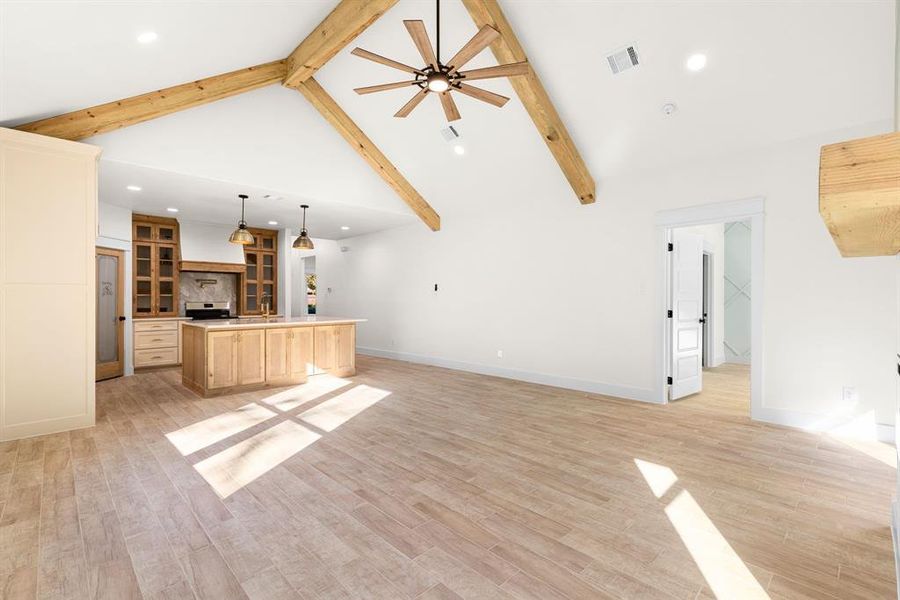 Unfurnished living room with beamed ceiling, light hardwood / wood-style floors, high vaulted ceiling, and ceiling fan