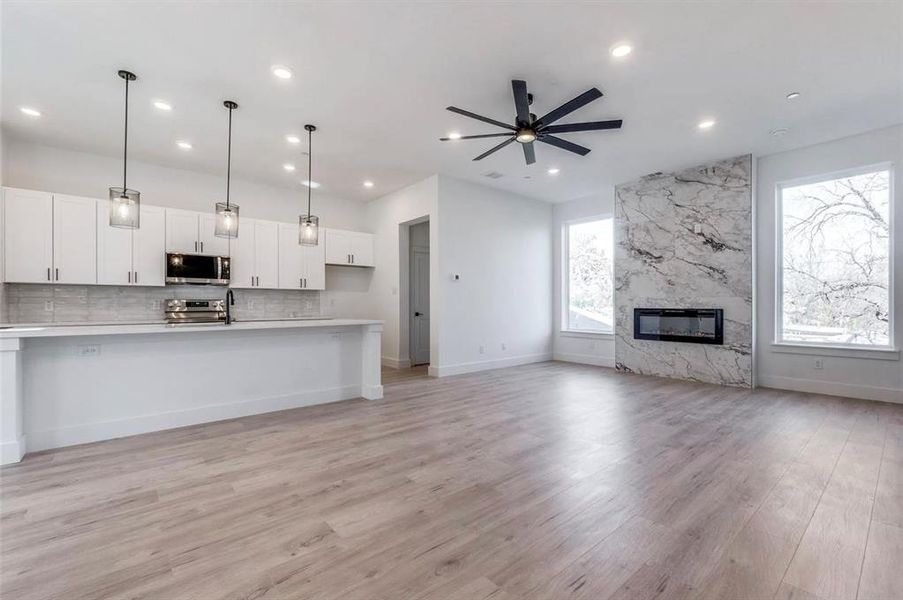 Kitchen with appliances with stainless steel finishes, white cabinets, a fireplace, pendant lighting, and ceiling fan