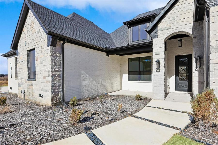 Property entrance with stone siding, roof with shingles, covered porch, and brick siding Property entrance with stone siding, roof with shingles, covered porch, and brick siding