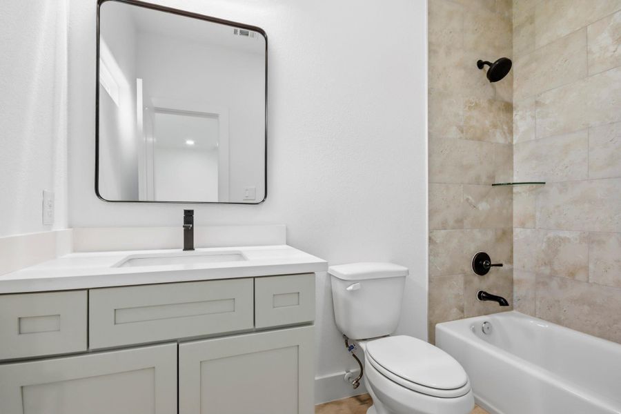 Modern secondary bathroom featuring sleek cabinetry, a stylish square mirror, and a chic tile shower with black fixtures.