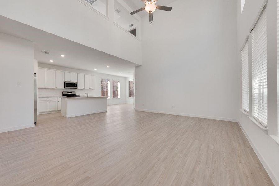 Unfurnished living room featuring a high ceiling, ceiling fan, and light wood finished floors Unfurnished living room featuring a high ceiling, ceiling fan, and light wood finished floors