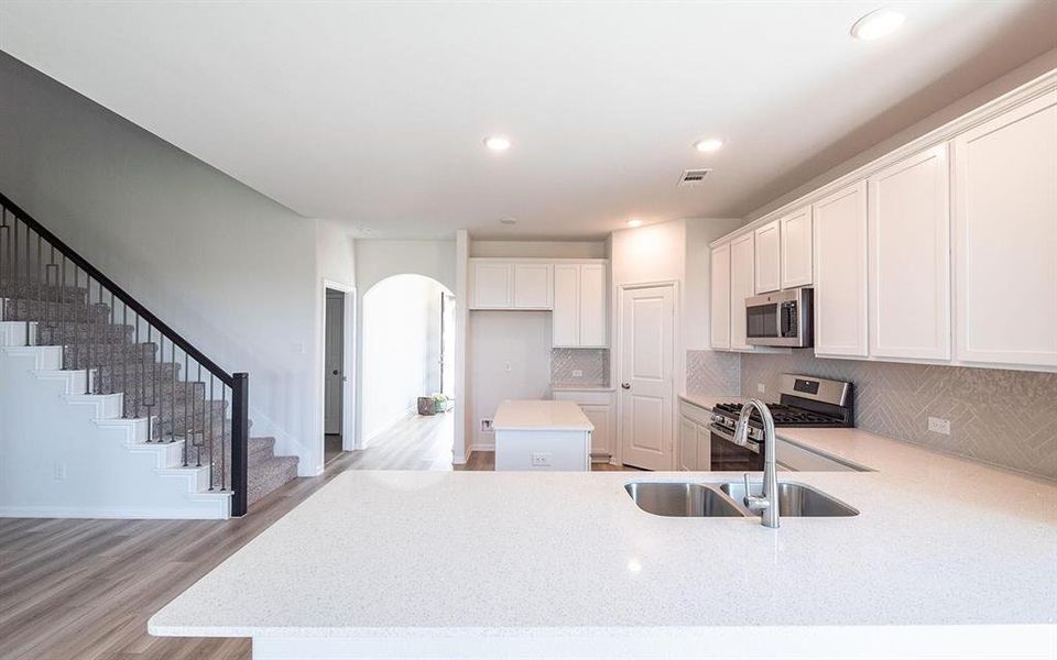 Kitchen with appliances with stainless steel finishes, light hardwood / wood-style flooring, sink, white cabinetry, and a kitchen island
