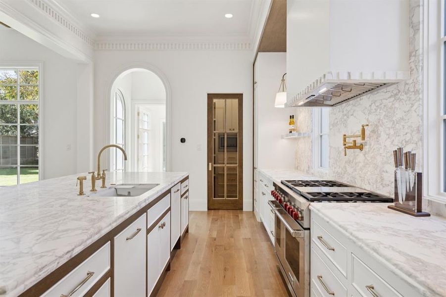 Kitchen with range with two ovens, white cabinets, custom range hood, light stone counters, and light wood-style floors