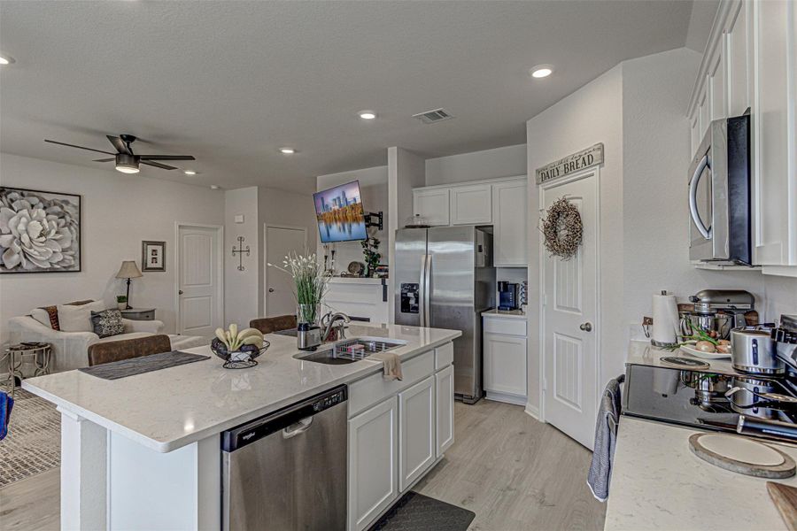 Kitchen with stainless steel appliances, open floor plan, white cabinets, light stone countertops, and a ceiling fan