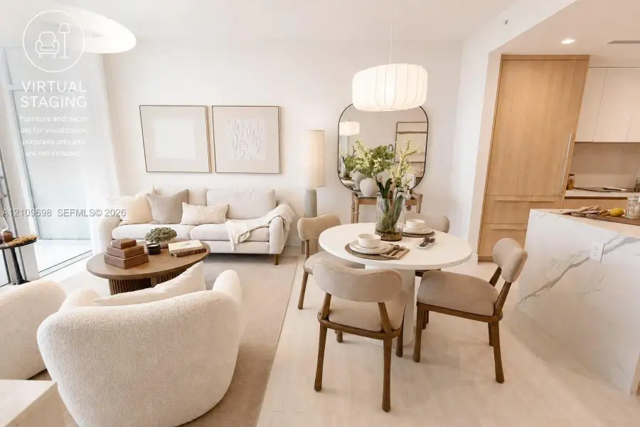 Open-concept interior featuring light-toned wood-finish flooring, a waterfall-edge stone island, built-in floor-to-ceiling cabinetry, and modern pendant lighting