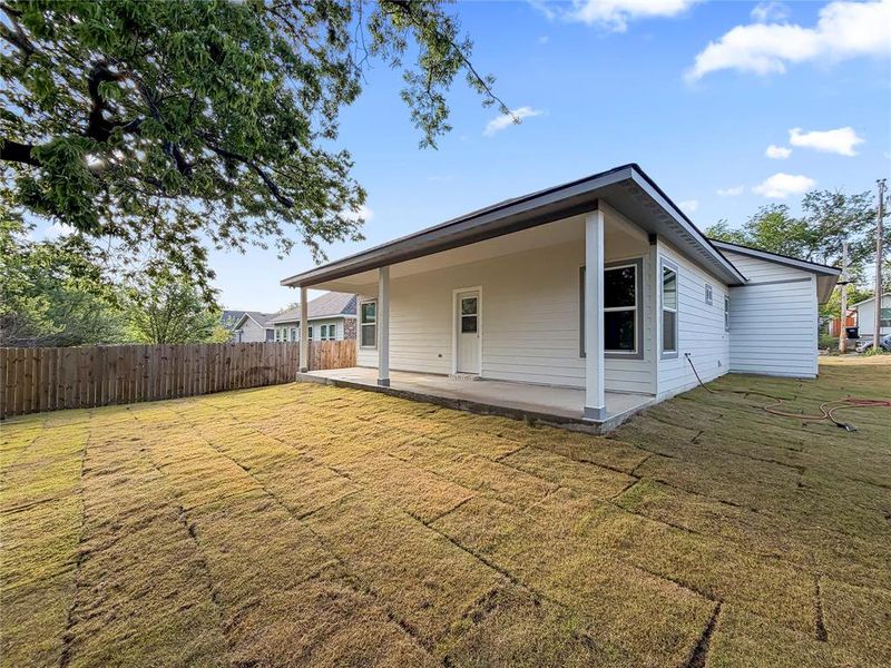 Expansive backyard featuring freshly laid sod, a full privacy fence, and a covered patio with light-toned siding and dark trim