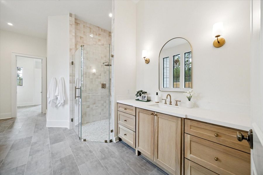 Elegant primary bath with dual vanities, frameless glass shower, custom designer lighting, and designer finishes.