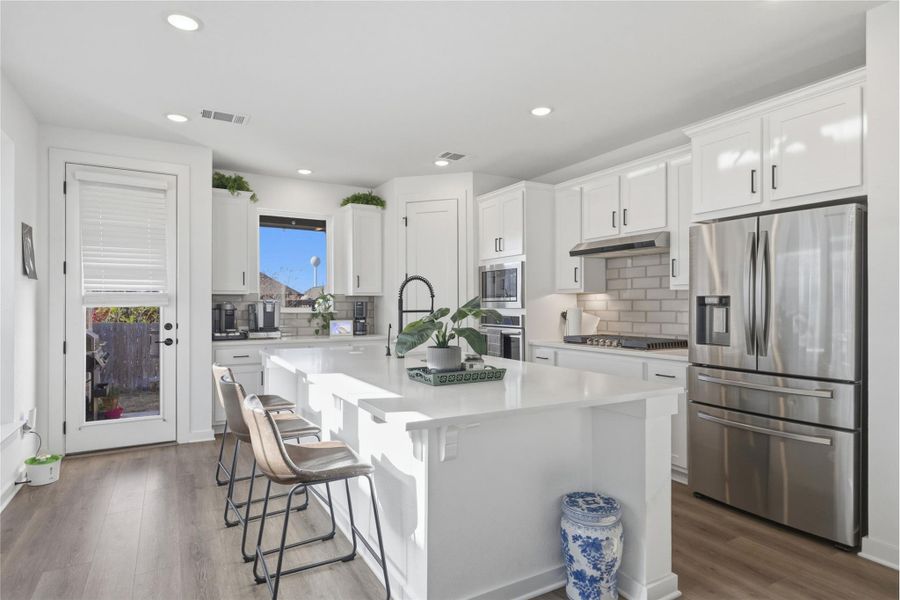 Kitchen featuring stainless steel appliances, decorative backsplash, white cabinetry, a kitchen island with sink, and recessed lighting