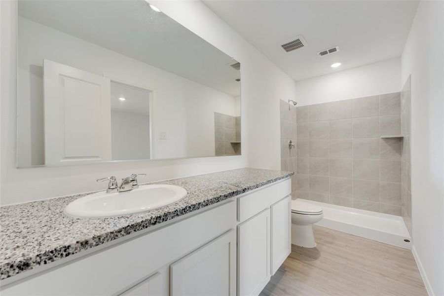 Bathroom with a tile shower, vanity, toilet, and hardwood / wood-style flooring