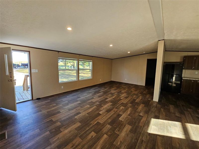 Unfurnished living room featuring dark wood-style flooring, a textured ceiling, recessed lighting, lofted ceiling, and crown molding Unfurnished living room featuring dark wood-style flooring, a textured ceiling, recessed lighting, lofted ceiling, and crown molding