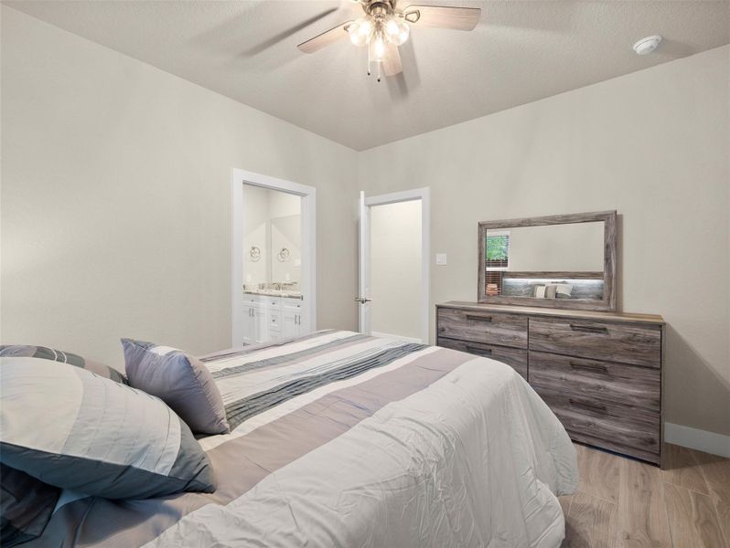 Bedroom featuring light wood finished floors, ceiling fan, and ensuite bath Bedroom featuring light wood finished floors, ceiling fan, and ensuite bath