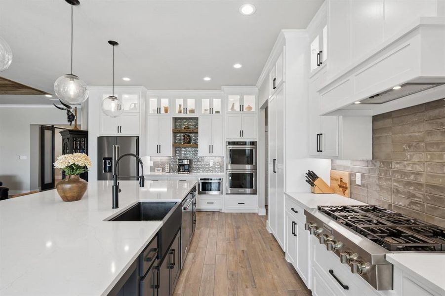 Dual tone kitchen with glass insert cabinets, stainless steel appliances, two tone cabinets, hanging light fixtures, and light wood finished floors
