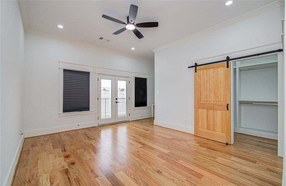 Primary bedroom features French doors with blackout blinds that leads to a covered balcony. A sliding barn door reveals a spacious walk-in closet.