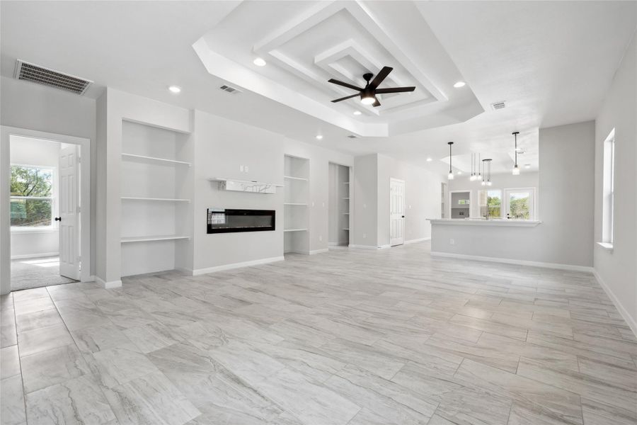 Unfurnished living room featuring built in features, healthy amount of natural light, baseboards, recessed lighting, and a tray ceiling Unfurnished living room featuring built in features, healthy amount of natural light, baseboards, recessed lighting, and a tray ceiling
