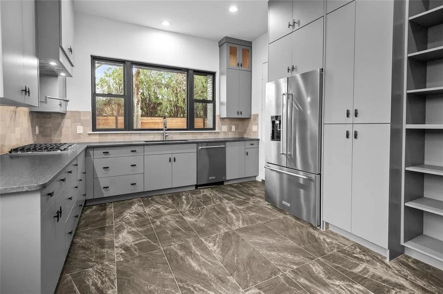 Modern kitchen featuring grey cabinetry, dark marble-finish flooring, and a large multi-pane window Modern kitchen featuring grey cabinetry, dark marble-finish flooring, and a large multi-pane window