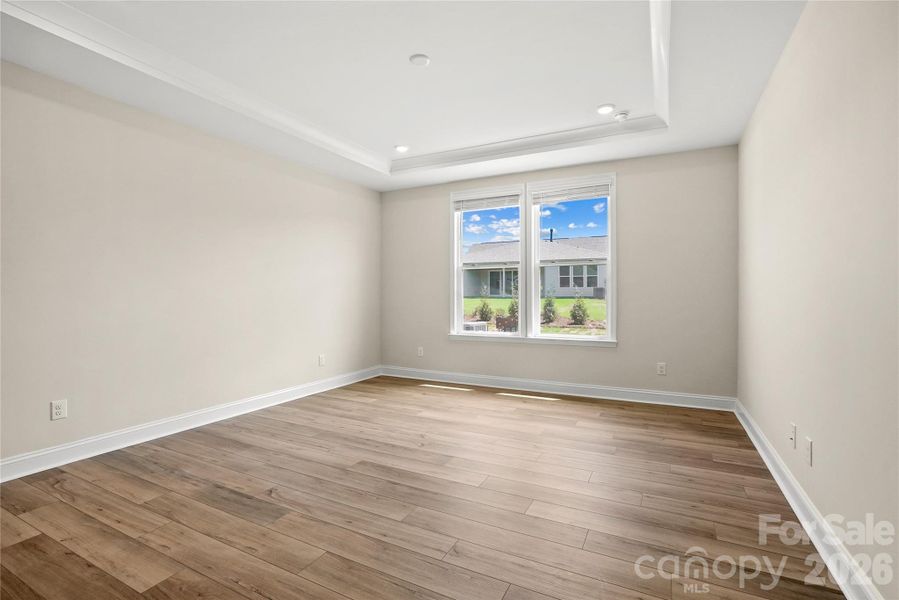 Large primary bedroom with tray ceiling, crown molding, and EVP flooring