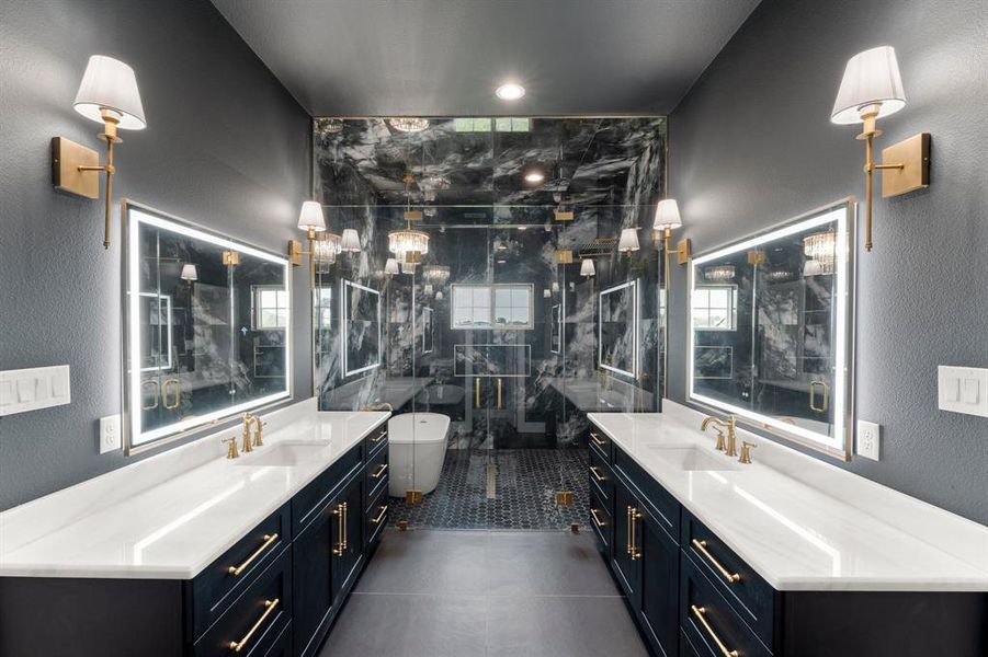 Bathroom featuring a textured wall, two vanities, a freestanding bath, a marble finish shower, and dark tile patterned floors