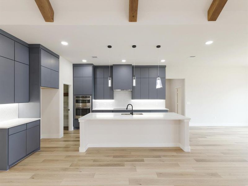 Kitchen with modern cabinets, a kitchen island with sink, light wood-style flooring, and decorative light fixtures