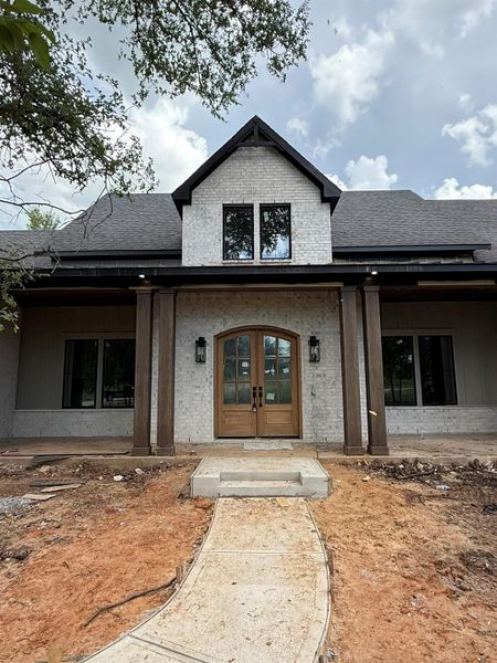 Doorway to property featuring french doors, a shingled roof, and brick siding