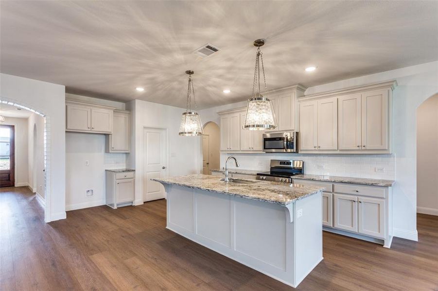 Kitchen featuring stainless steel appliances, a center island with sink, sink, dark hardwood / wood-style floors, and pendant lighting