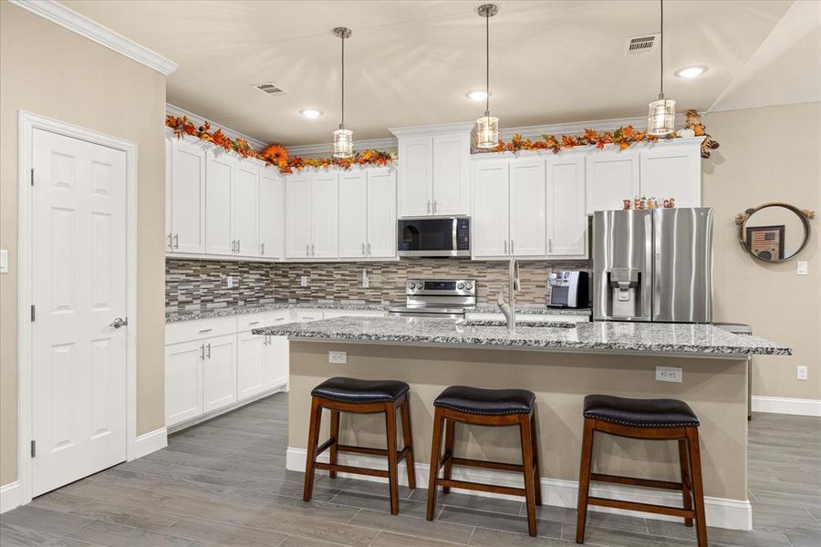 Kitchen featuring stainless steel appliances, a breakfast bar area, decorative backsplash, pendant lighting, and light stone counters Kitchen featuring stainless steel appliances, a breakfast bar area, decorative backsplash, pendant lighting, and light stone counters