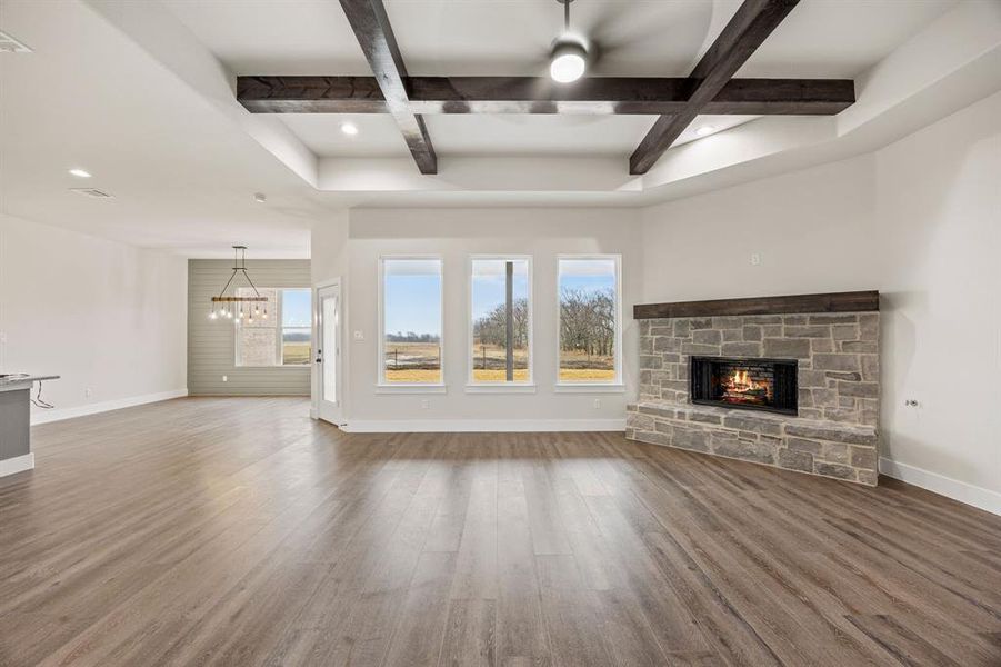 Unfurnished living room with coffered ceiling, a stone fireplace, dark wood-style floors, hanging lights, and plenty of natural light Unfurnished living room with coffered ceiling, a stone fireplace, dark wood-style floors, hanging lights, and plenty of natural light