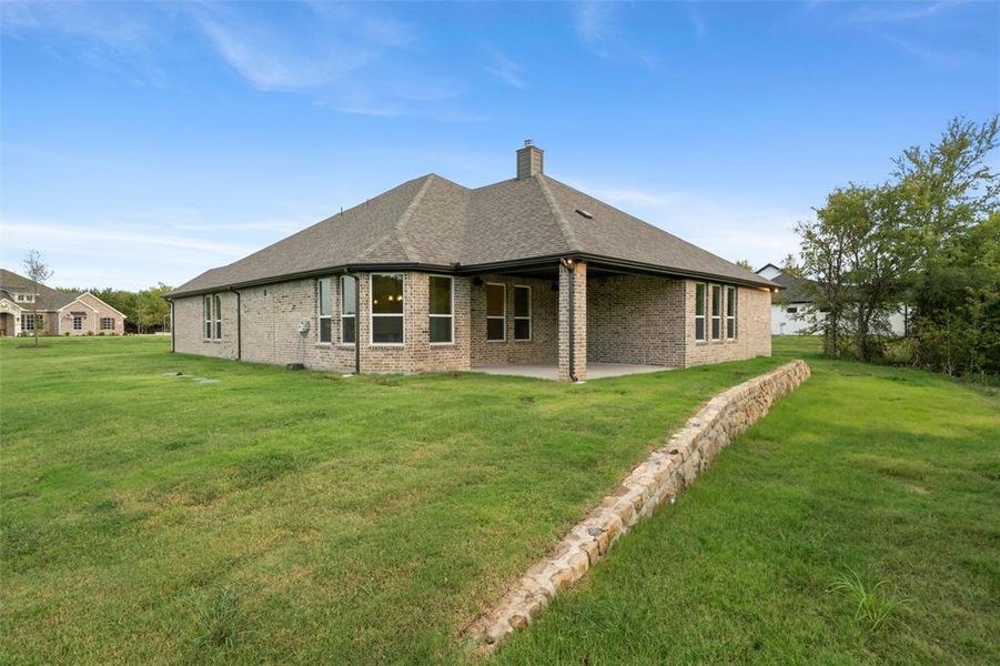 Back of house with a shingled roof, brick siding, a yard, a patio, and a chimney