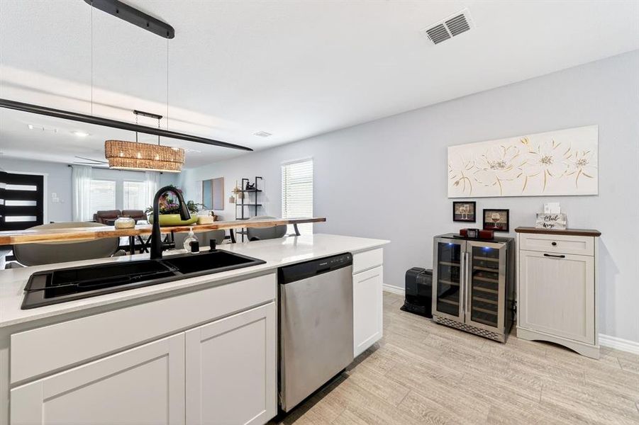 Kitchen island featuring a black undermount sink with a gooseneck faucet, light-colored countertops, white cabinetry, and a stainless steel dishwasher