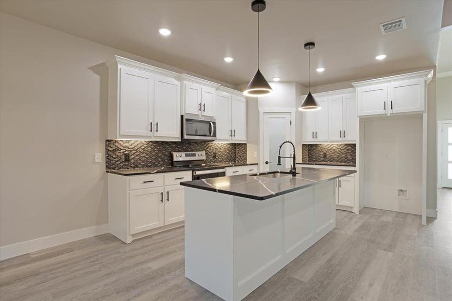 Kitchen with an island with sink, sink, pendant lighting, light wood-type flooring, and appliances with stainless steel finishes