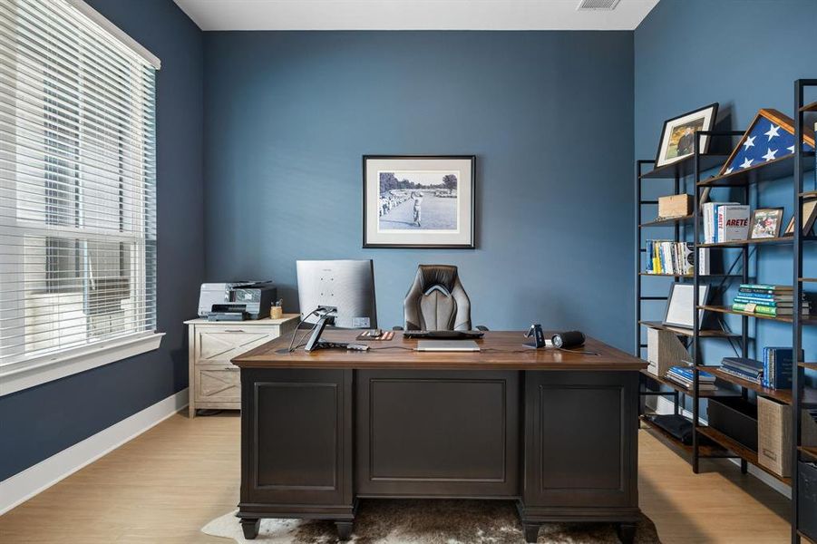 Dedicated office space featuring light wood-finish flooring, a window with horizontal blinds, and a built-in shelving unit Dedicated office space featuring light wood-finish flooring, a window with horizontal blinds, and a built-in shelving unit